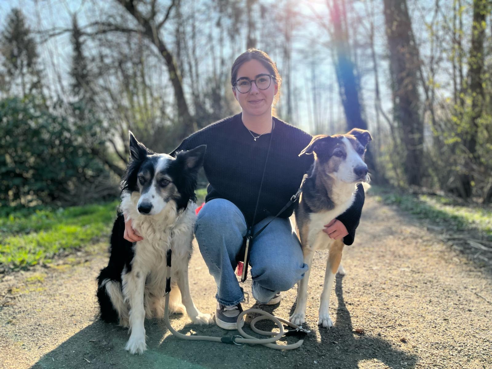 Frau mit Brille kniet auf Waldweg zwischen zwei Hunden